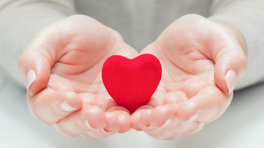 Small red heart in woman's hands in a gesture of giving, protecting
